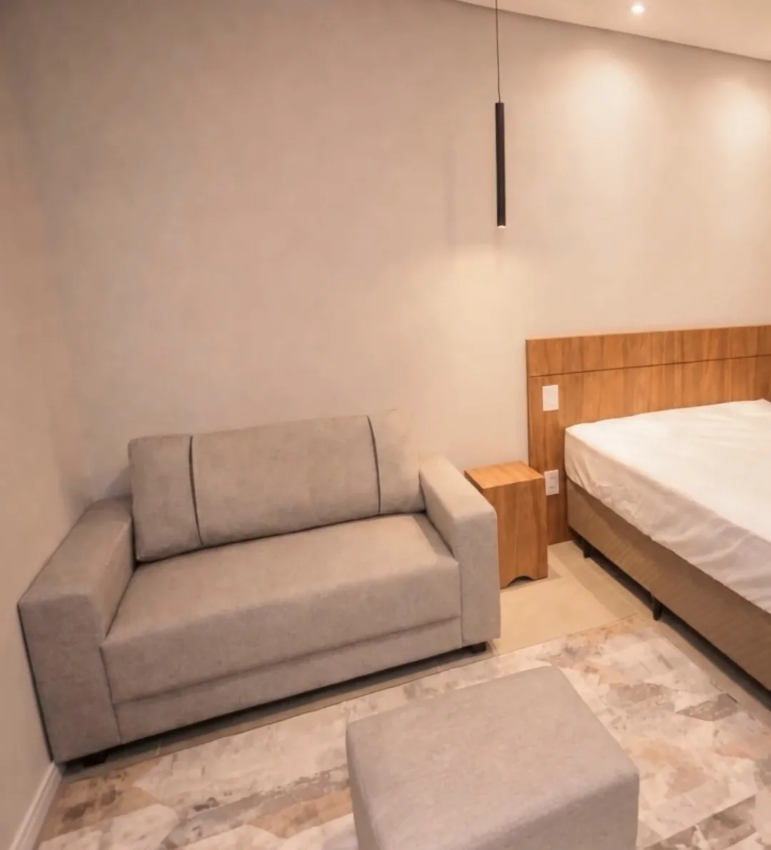 Studio mobiliado por dentro: sofá, cama de casal com cabeceira de madeira e piso claro.